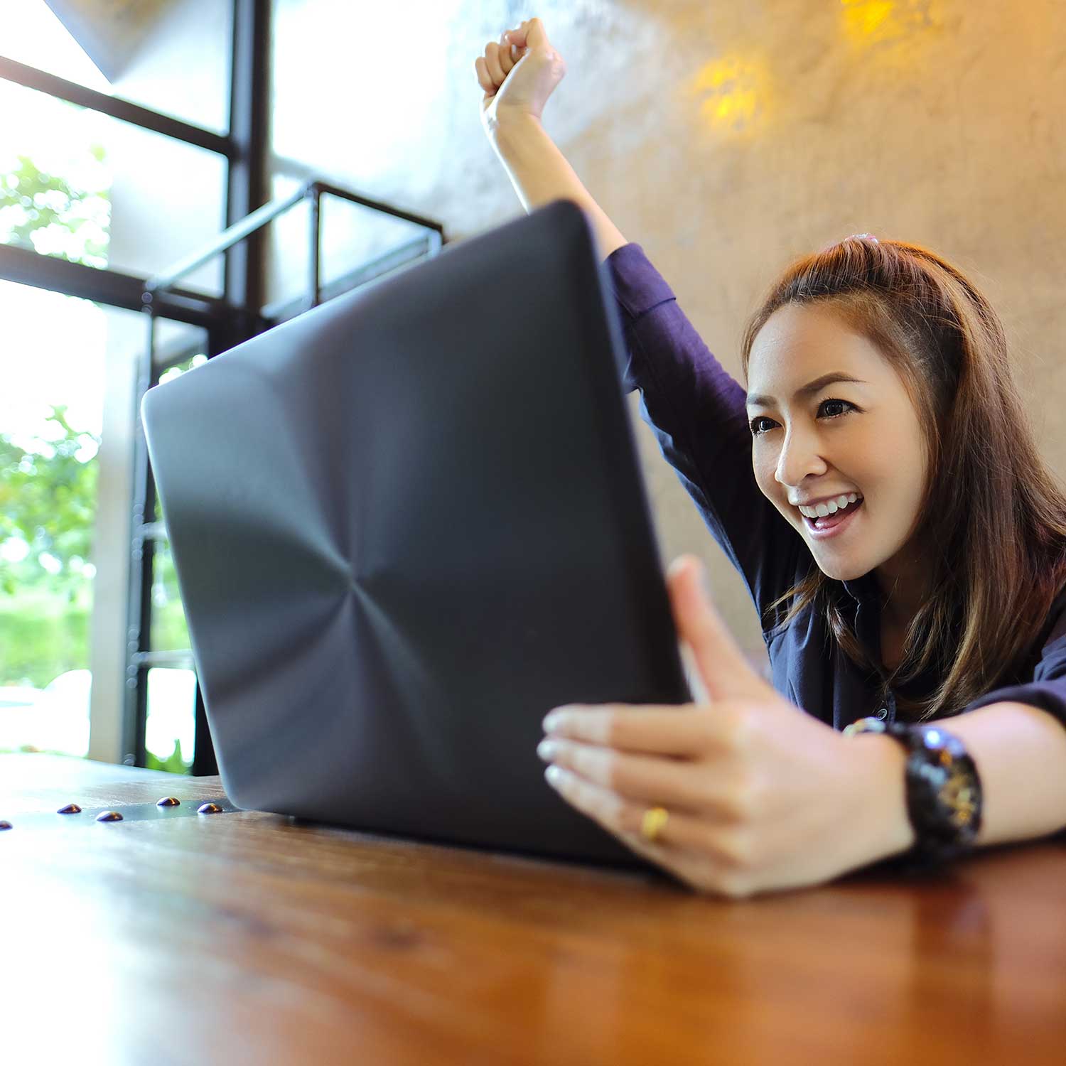 a young woman holds up her hand to cheer while looking at a laptop